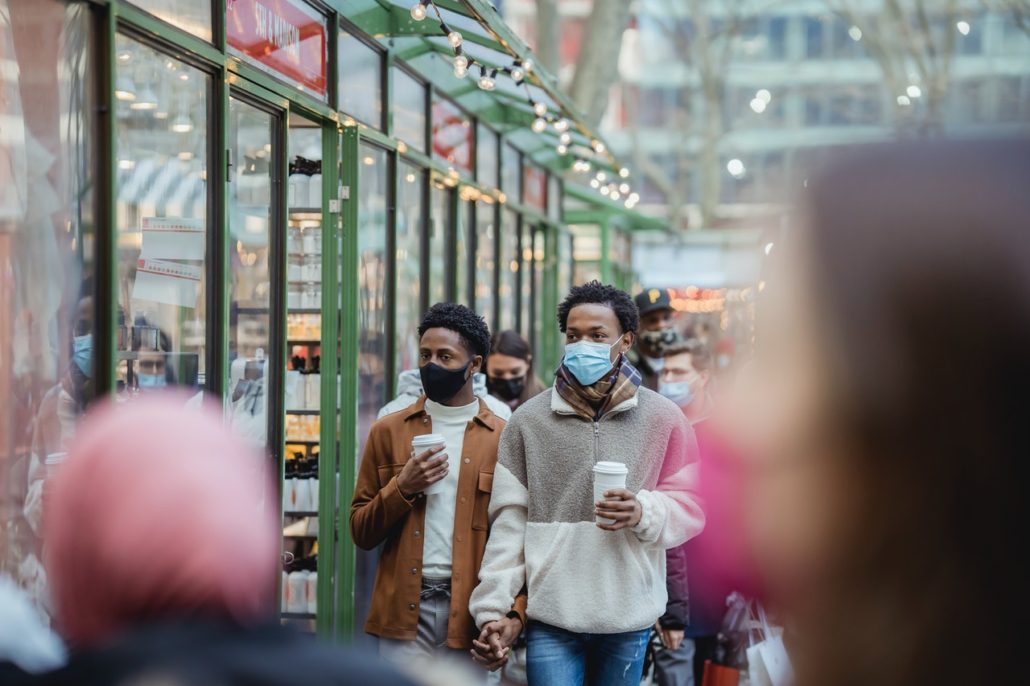 black couple walking down a crowded street wearing masks